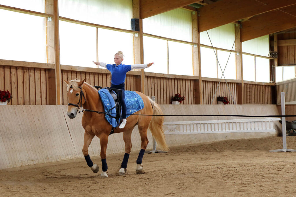Dziewczynka trenująca woltyżerkę na lonżowanym koniu